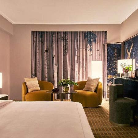 Hotel Park Lane New York Esterno foto The photo shows a stylish hotel room featuring a king-sized bed with a white duvet in the foreground. In the background, there are two contemporary armchairs in a warm yellow color, positioned around a small round table with a floral arrangement. A l