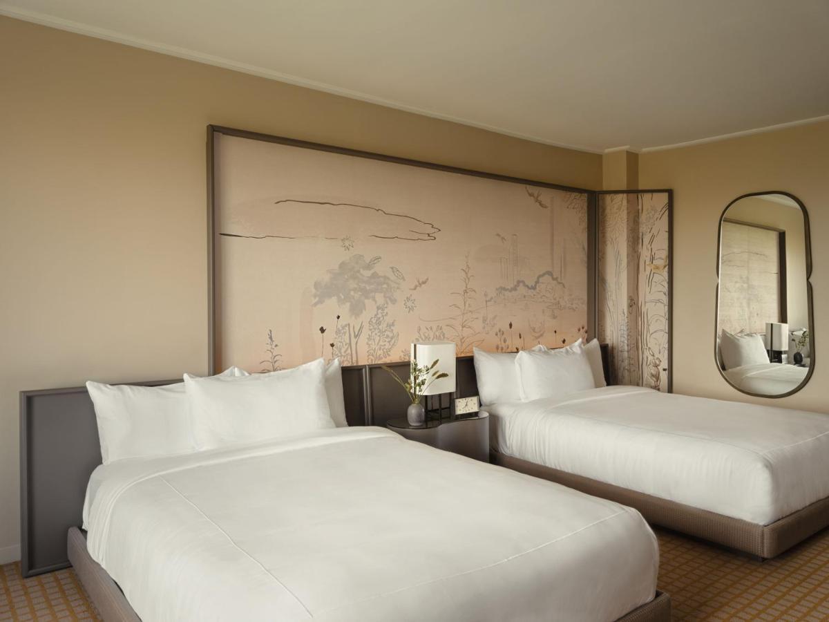 Hotel Park Lane New York Esterno foto The photo shows a modern hotel room featuring two beds with white linens. The background has a large wall art piece that seems to depict a subtle landscape or abstract design. There is a nightstand between the beds with a small decorative item, possi