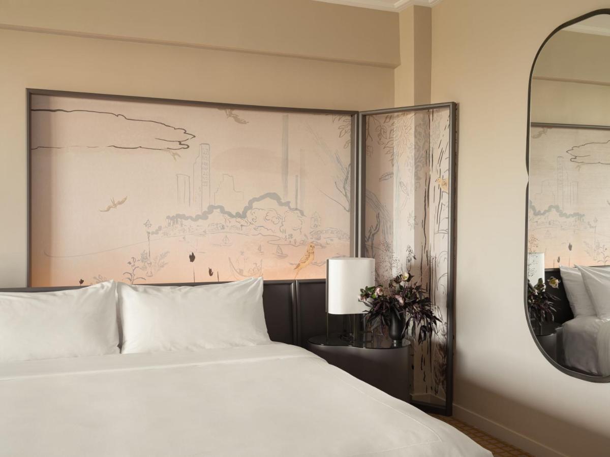 Hotel Park Lane New York Esterno foto The photo shows a modern bedroom featuring a large, neatly made bed with white bedding. Behind the bed is a decorative feature wall illustrated with soft, muted patterns, possibly depicting a landscape or abstract design. To the side, there's a lamp 