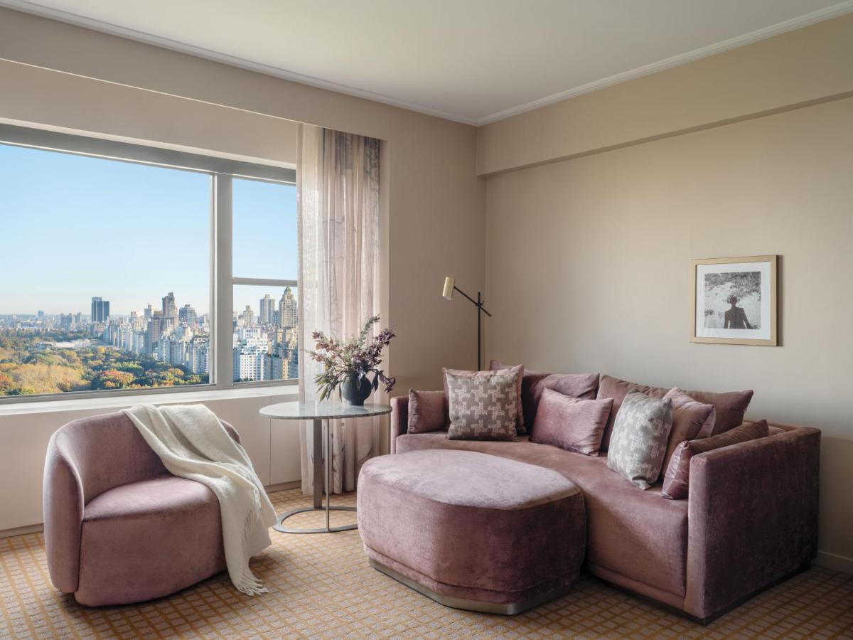 Hotel Park Lane New York Esterno foto The photo shows a modern, cozy interior of a living space. It features a plush, curved sofa in soft purple tones, accompanied by a round chair in a similar color. There is a small, round side table with a vase of flowers on it. A light-colored throw 