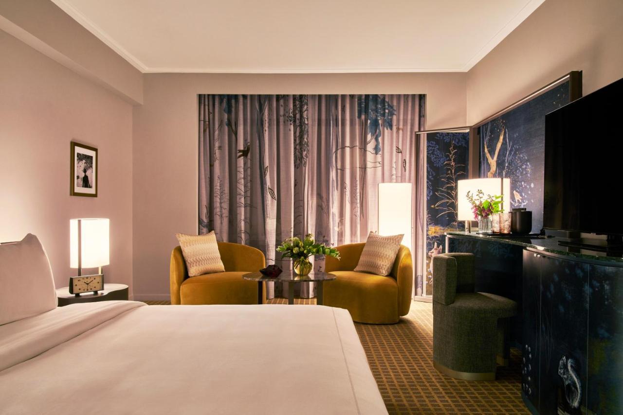 Hotel Park Lane New York Esterno foto The photo shows a stylish hotel room featuring a king-sized bed with a white duvet in the foreground. In the background, there are two contemporary armchairs in a warm yellow color, positioned around a small round table with a floral arrangement. A l