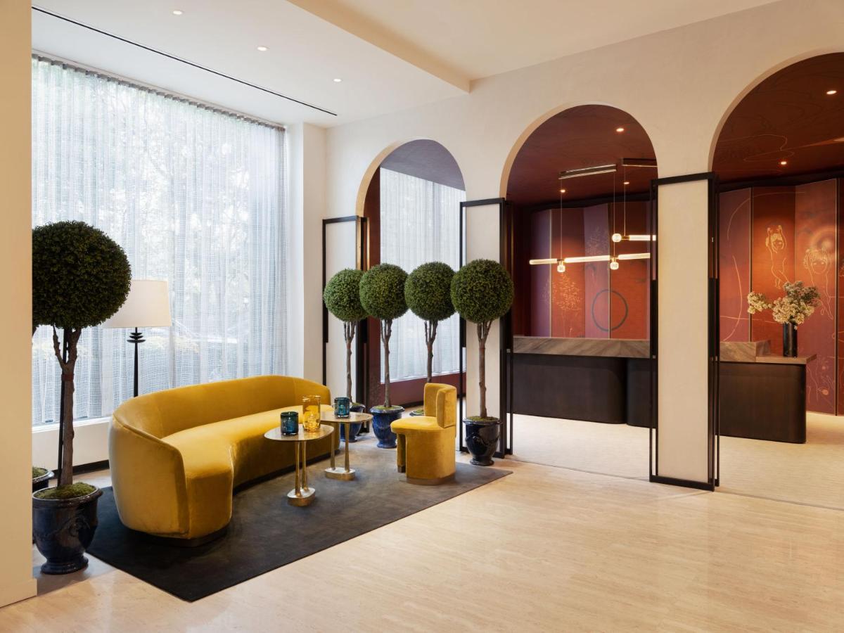 Hotel Park Lane New York Esterno foto The photo depicts a modern interior space, likely a lobby or lounge area. It features a stylish, curved yellow sofa complemented by two smaller yellow chairs. The floor is adorned with a dark rug, and there are small round tables with decorative item