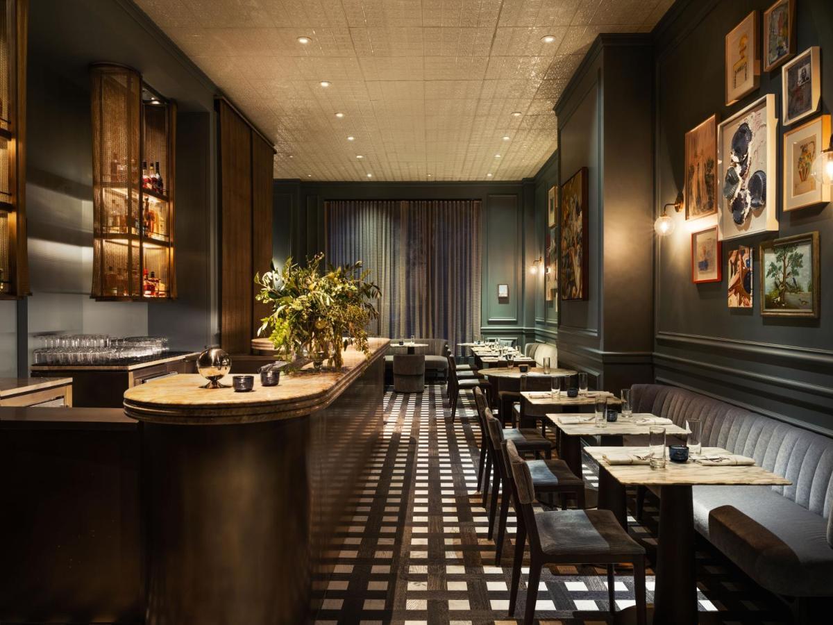 Hotel Park Lane New York Esterno foto The photo shows a stylish restaurant interior. There is a bar area with a rounded countertop, and behind it, there are shelves displaying various items. The seating includes both a long, cushioned booth along the wall and individual tables with chair
