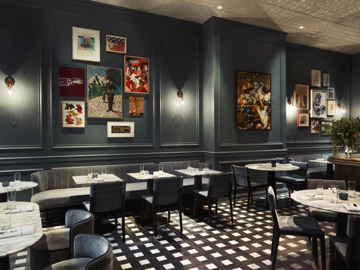 Hotel Park Lane New York Esterno foto The photo displays a stylish restaurant interior. The walls are painted a deep blue and adorned with a variety of framed artworks in different styles and sizes. There are several tables set with white tablecloths, and black chairs are arranged around