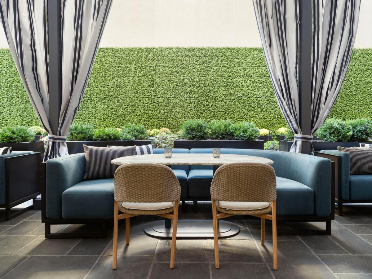 Hotel Park Lane New York Esterno foto The photo shows a modern outdoor seating area. There are two chairs positioned around a small table, with a plush blue sofa in the background. The sofa has cushions and is set against a backdrop of greenery, including potted plants or hedges. The are
