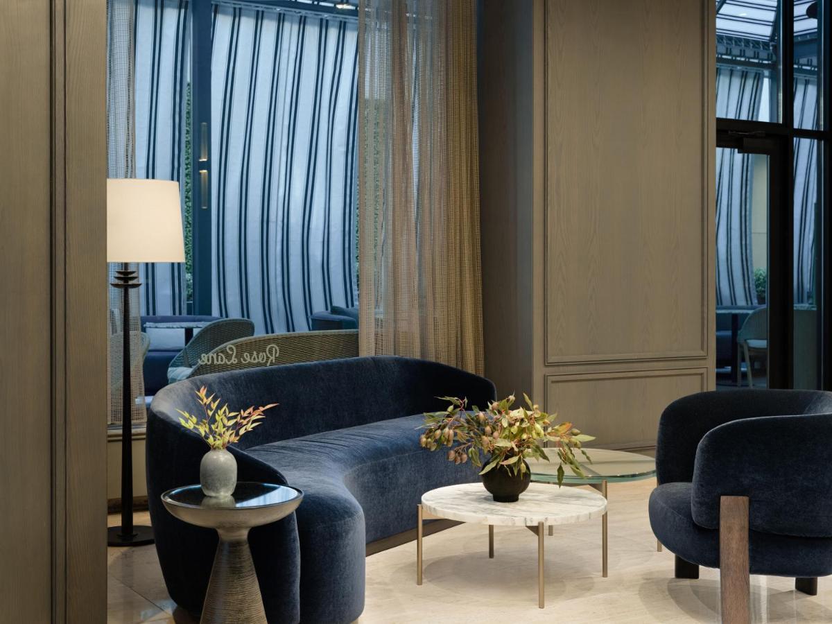 Hotel Park Lane New York Esterno foto The photo shows a stylish and modern interior space. There is a curved blue sofa and two round chairs, all with a plush design. A small round table with a floral arrangement sits in the center. In the background, large windows are covered with light,