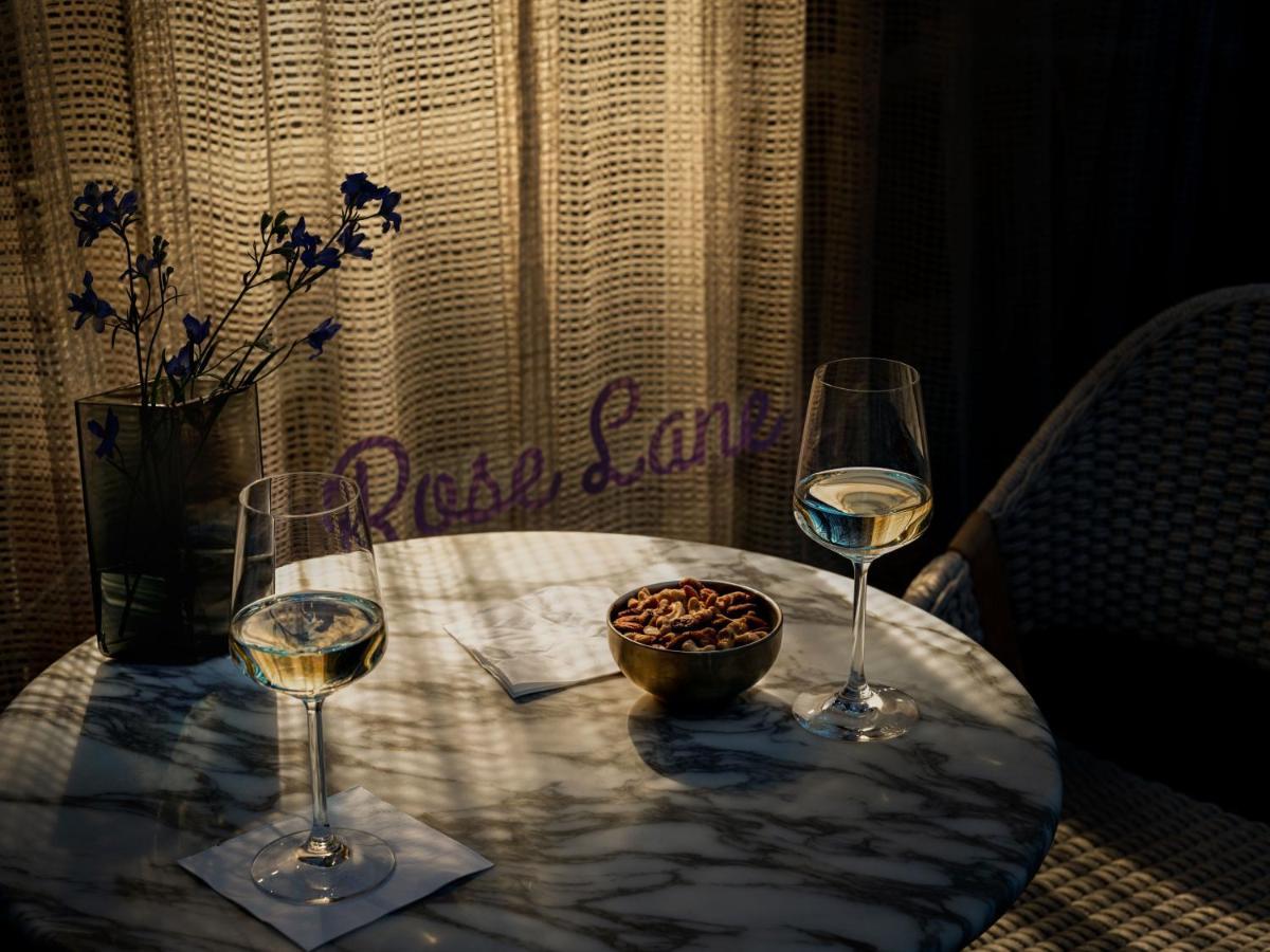 Hotel Park Lane New York Esterno foto The photo shows a cozy setting featuring a marble table with two glasses of white wine. There is a small bowl of nuts on the table, accompanied by two coasters. In the background, a decorative pot contains some flowers, and a textured curtain lets in