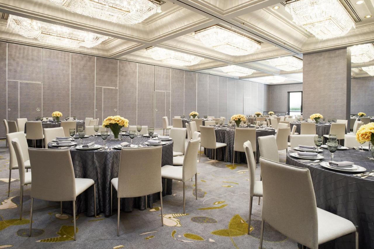 Hotel Park Lane New York Esterno foto The photo depicts an elegant dining or event space. It features several round tables covered with gray tablecloths, each set with plates, glasses, and silverware. Centerpieces of yellow flowers are arranged on most tables. The room has modern, white 
