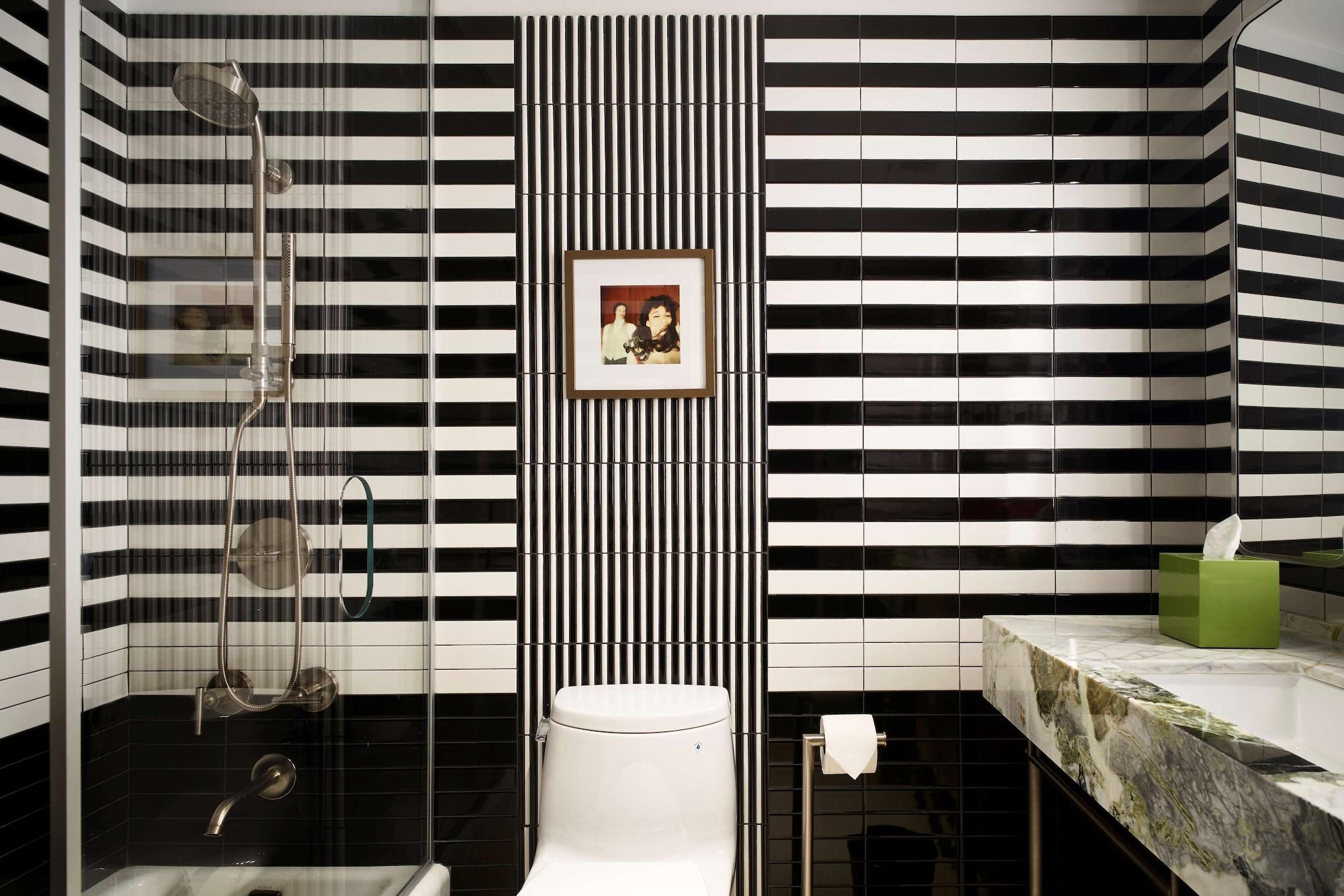 Hotel Park Lane New York Esterno foto The photo shows a modern bathroom featuring a striking design with black and white striped tiles on the walls. There is a glass shower enclosure on one side, and a white toilet sits against the wall. Above the toilet, there is a small framed picture 