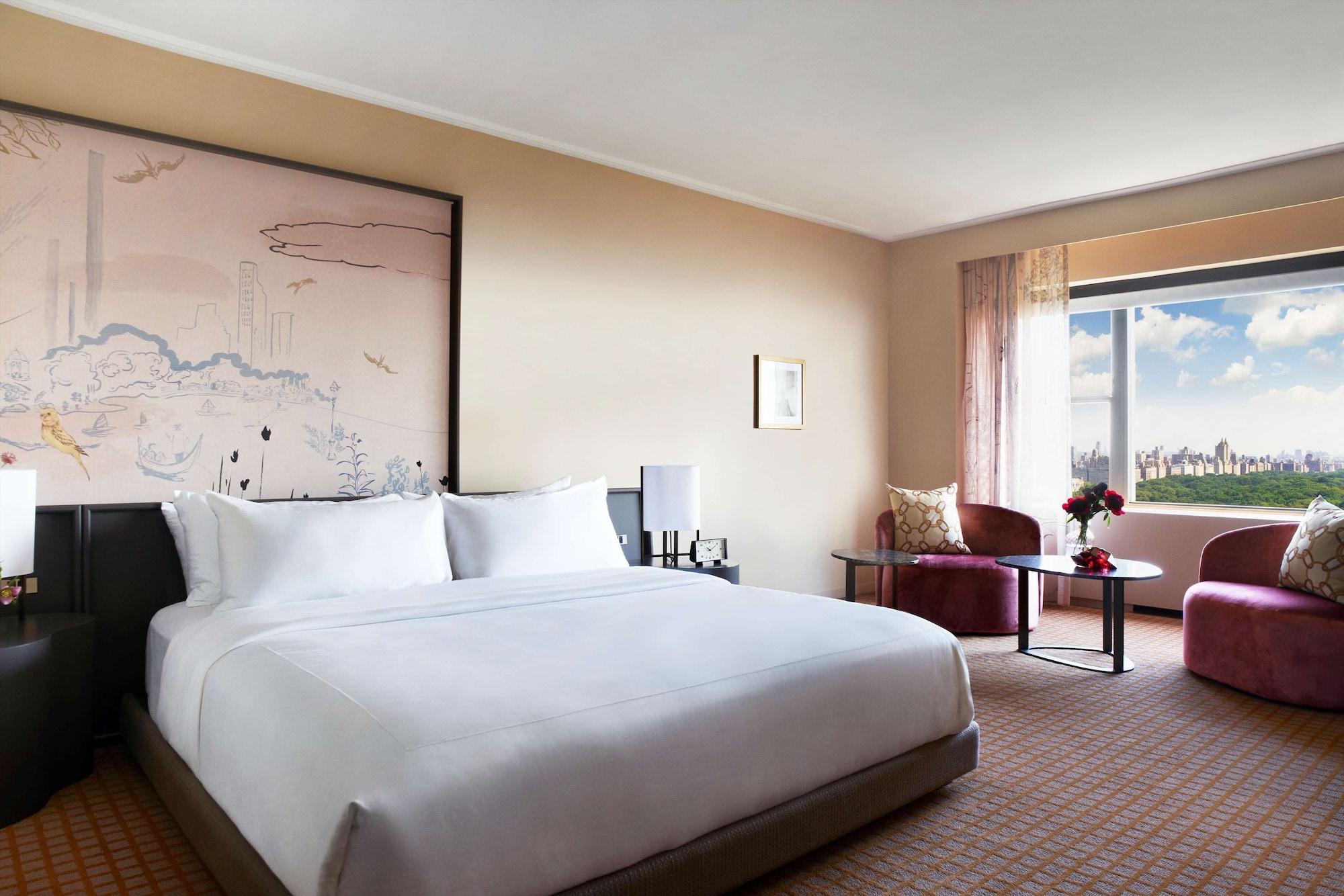 Hotel Park Lane New York Esterno foto The photo shows a well-appointed hotel room featuring a large, neatly made bed with white linens. Behind the bed is a decorative wall art piece, possibly featuring a landscape or abstract design. To one side of the room, there's a seating area that i
