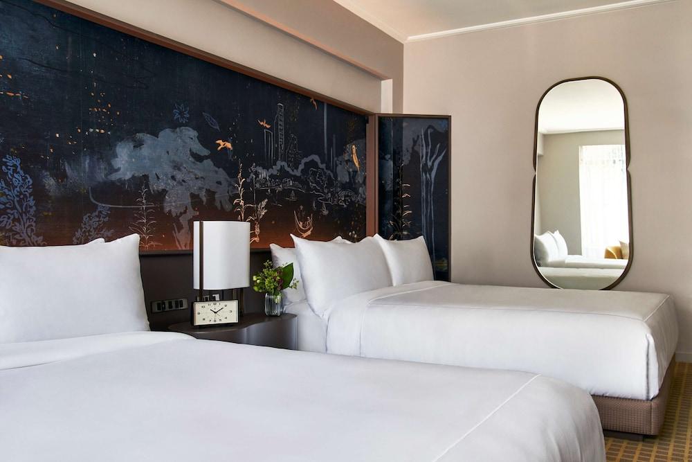 Hotel Park Lane New York Esterno foto The photo depicts a modern hotel room featuring two white beds with neatly arranged bedding. Behind the beds is an artistic wall with a dark, scenic mural, which adds a touch of elegance to the space. There is a bedside table with a clock and a small