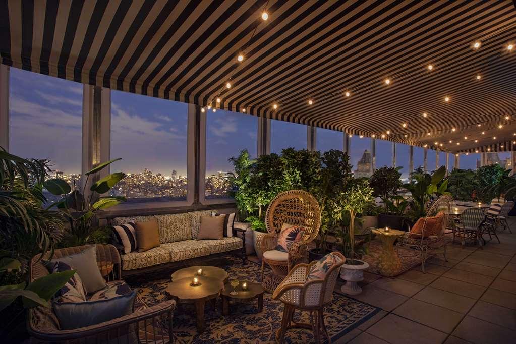 Hotel Park Lane New York Ristorante foto The photo depicts a stylish rooftop lounge area with a modern and cozy atmosphere. The space features a striped awning overhead, providing shade and a decorative touch. Soft lighting from hanging bulbs creates a warm ambiance as evening approaches. 
