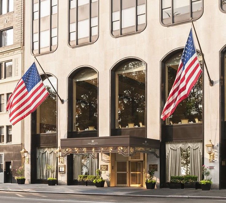 Hotel Park Lane New York Esterno foto The photo shows the exterior of a building, likely a hotel or an upscale establishment. There are two large American flags displayed prominently on either side of the entrance. The entrance features a golden door and decorative elements, while the wi