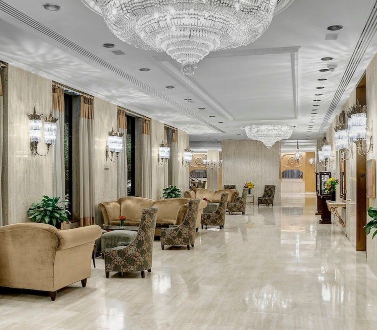 Hotel Park Lane New York Esterno foto The image shows an elegant hotel lobby or lounge area. It features a polished marble floor and is decorated with soft, neutral-colored walls. The space is illuminated by several large chandeliers hanging from the ceiling and sconces mounted on the wa