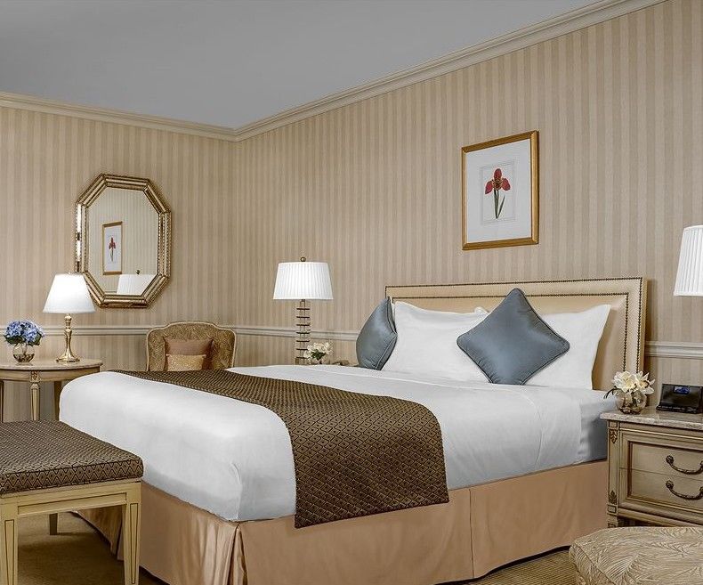 Hotel Park Lane New York Esterno foto The photo shows a well-decorated hotel room featuring a neatly made king-sized bed. The bed has a light-colored comforter with decorative pillows in shades of blue. On either side of the bed, there are bedside tables with lamps providing soft lightin