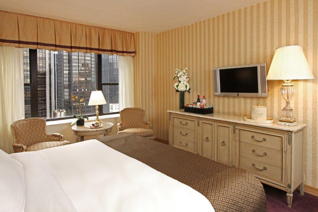Hotel Park Lane New York Esterno foto The image shows a hotel room with a cozy and inviting atmosphere. There is a large bed with white bedding, and the walls are decorated with striped wallpaper in soft colors. A pair of armchairs sits next to a small table near a window, which allows n