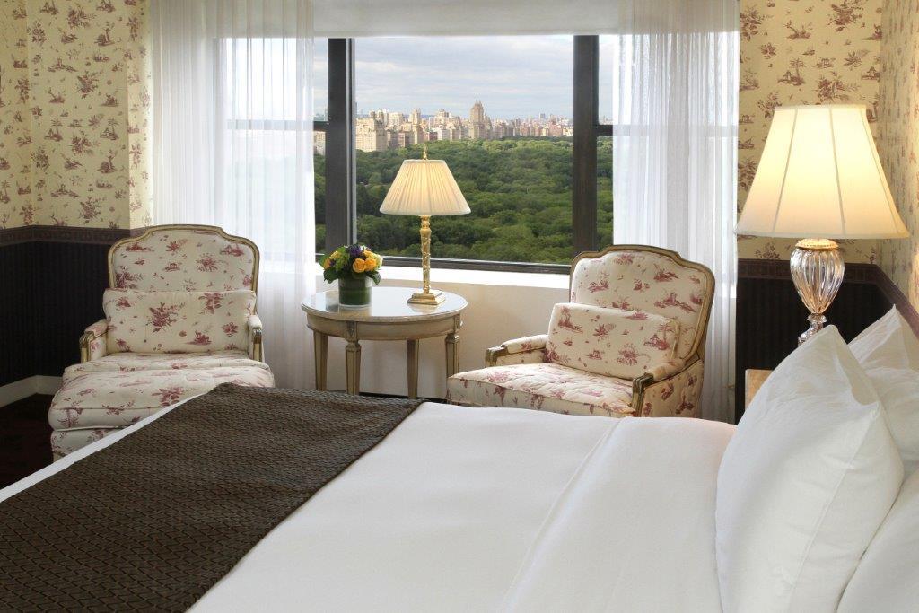 Hotel Park Lane New York Esterno foto The photo shows a well-decorated hotel room. In the foreground, there's a neatly made bed with a white bedspread. To the side, there are two elegant chairs with floral patterns, positioned near a small round table. A lamp sits on the table, and there