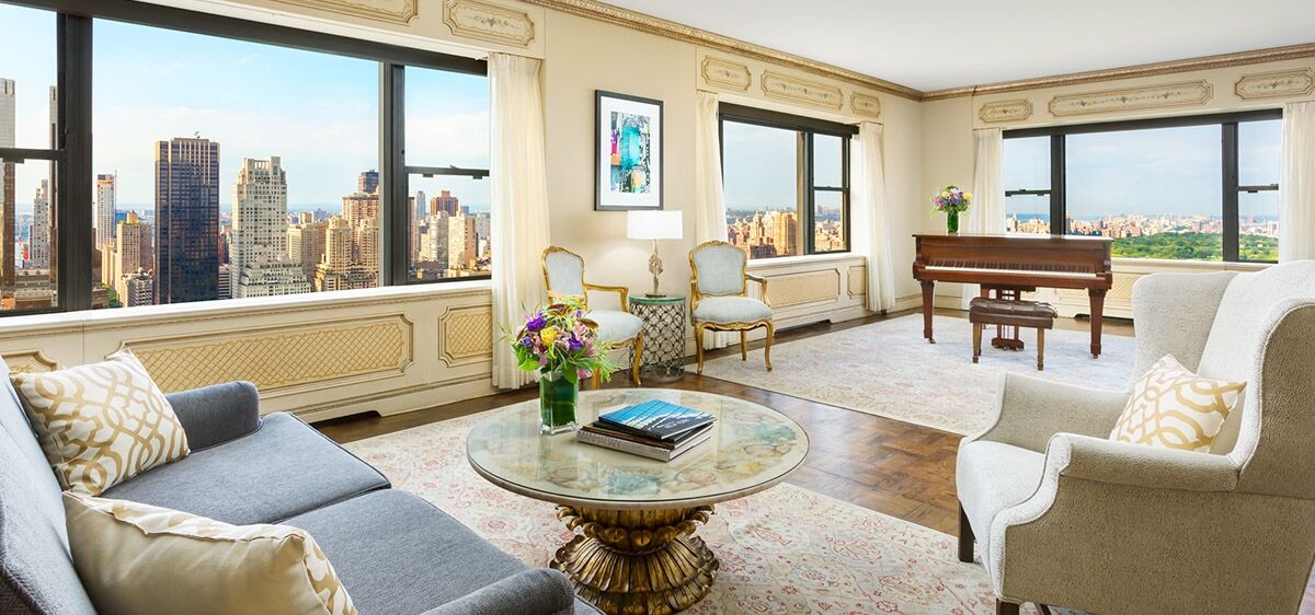 Hotel Park Lane New York Esterno foto The photo shows a stylish and elegant living room with large windows that offer a view of a cityscape. The decor includes a comfortable gray sofa and two light-colored armchairs. In the center, there is a round coffee table with a decorative base and