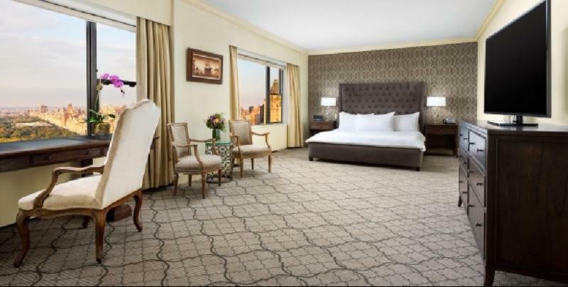 Hotel Park Lane New York Esterno foto The photo shows a spacious hotel room featuring a large bed with white bedding. There are two elegant chairs and a small table, likely used for seating or relaxation. The room has large windows with curtains that allow natural light to enter, and the