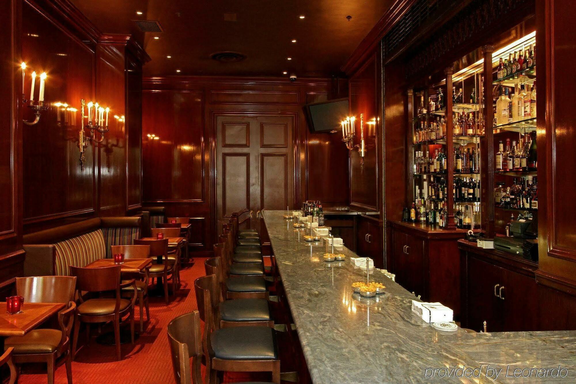 Hotel Park Lane New York Ristorante foto The photo shows the interior of a bar. It features a long, polished marble bar top with several bar stools lined up in front. The walls are paneled in rich, dark wood, and there are elegant sconces providing soft lighting. Behind the bar, a well-stoc