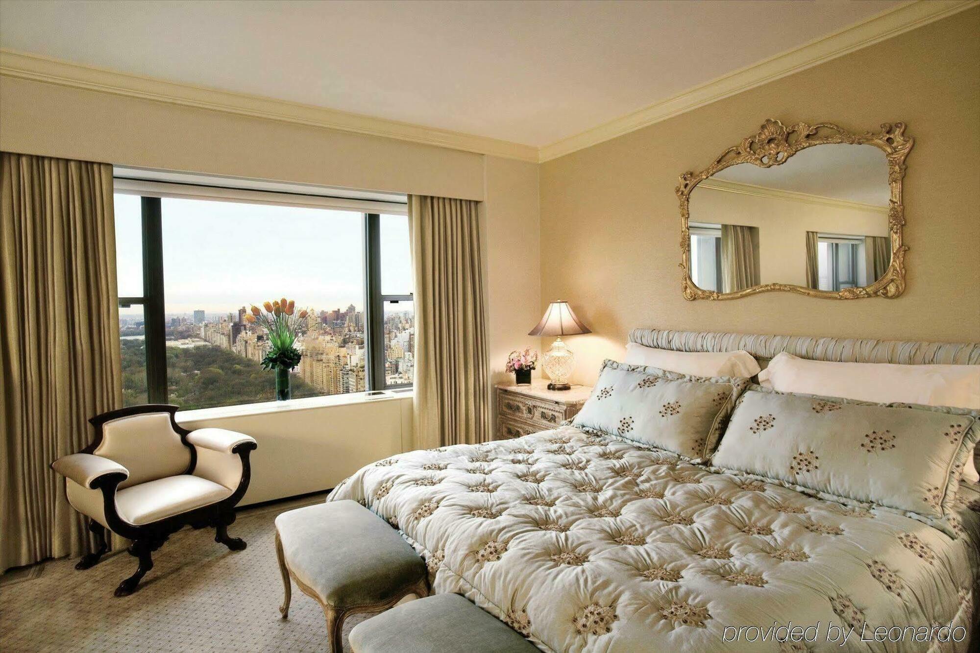 Hotel Park Lane New York Camera foto The photo depicts a cozy, elegantly decorated bedroom. The focal point is a large bed with a luxurious, tufted comforter featuring floral patterns. To the side of the bed, there's a small upholstered bench. There's a window with stylish drapes, offer